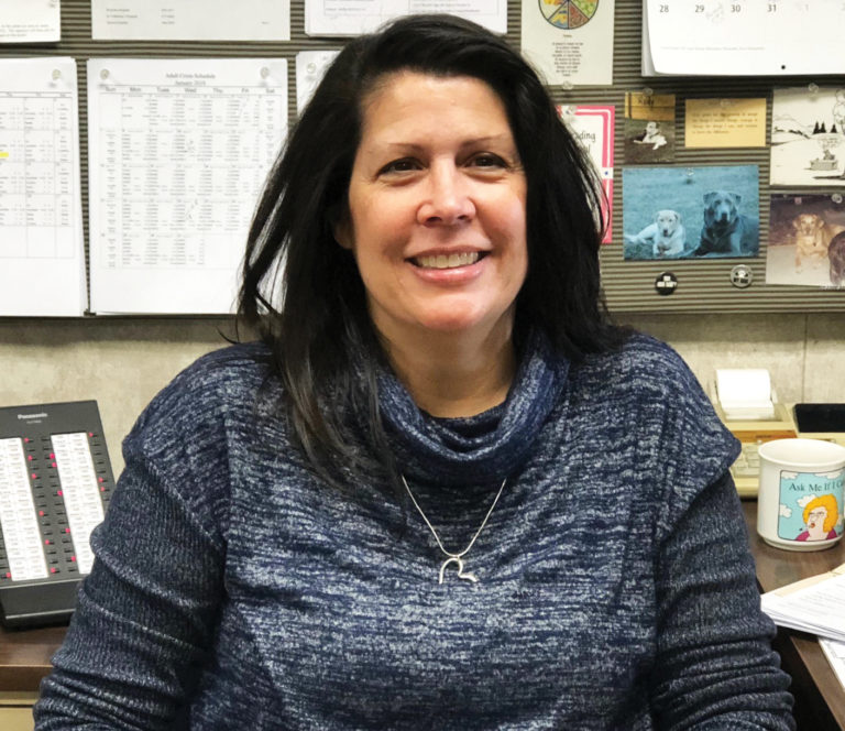 Gina sitting at work wearing a grey and blue shirt.