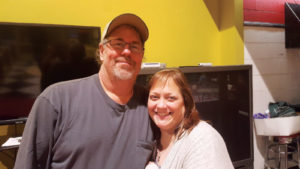 Ken Korp wearing a blue shirt and baseball cap standing next to Kat Korp in a gray sweater.